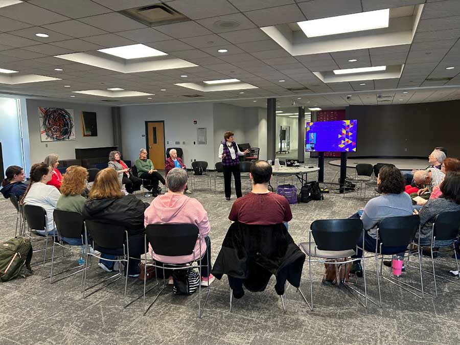 large group sitting in a circle listening to a woman speak