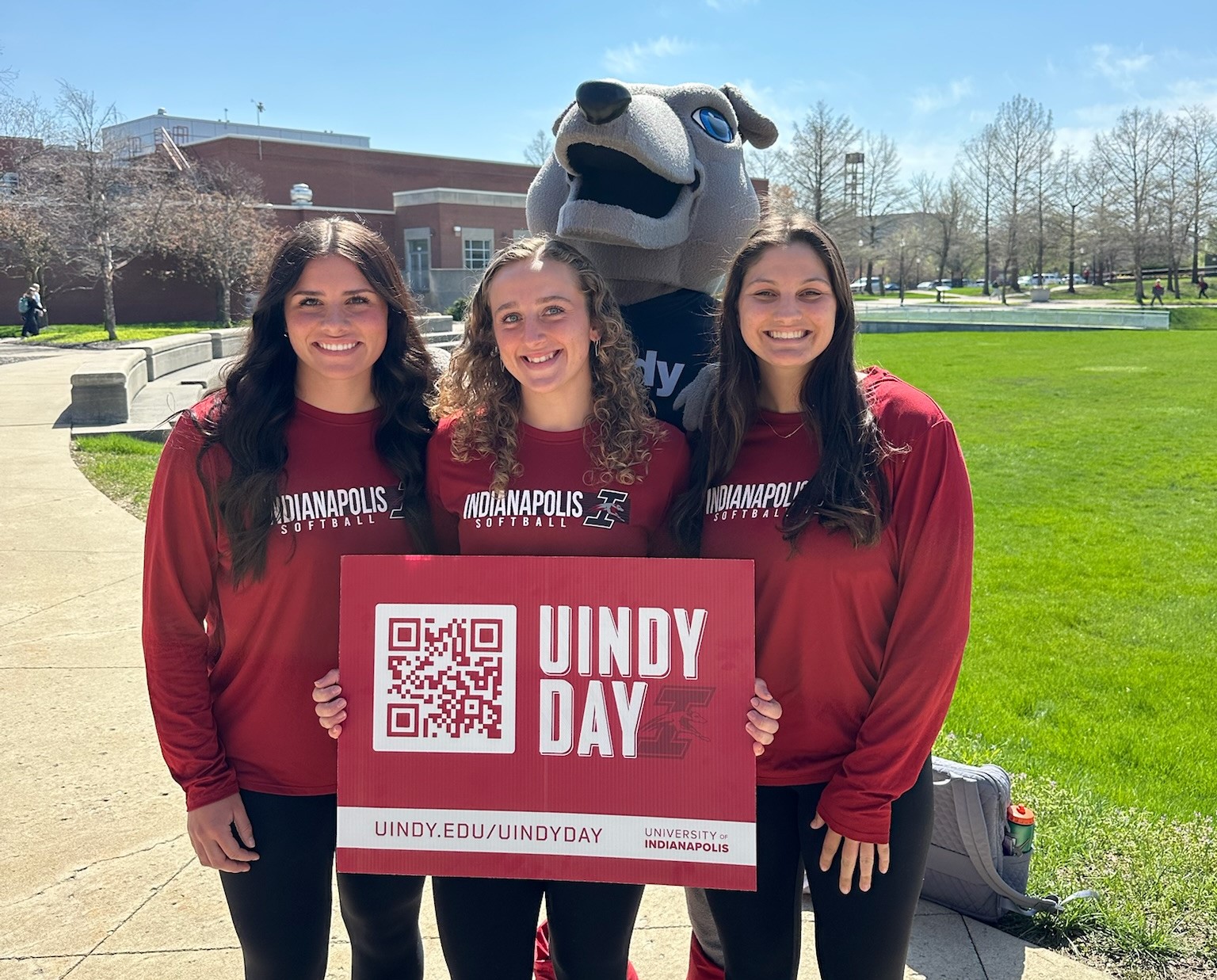 A group of UIndy students posing on Smith Mall with the UIndy costume mascot, Ace, holding a UIndy Day sign.
