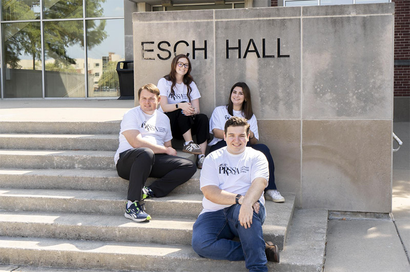 four students sitting on the steps in front of Esch Hall
