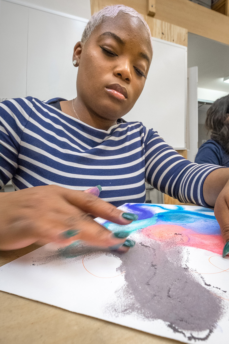 a student using her hands to create artwork on a canvas