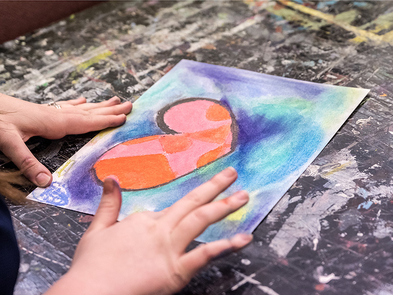 a pair of hands creating artwork on paper with a heart