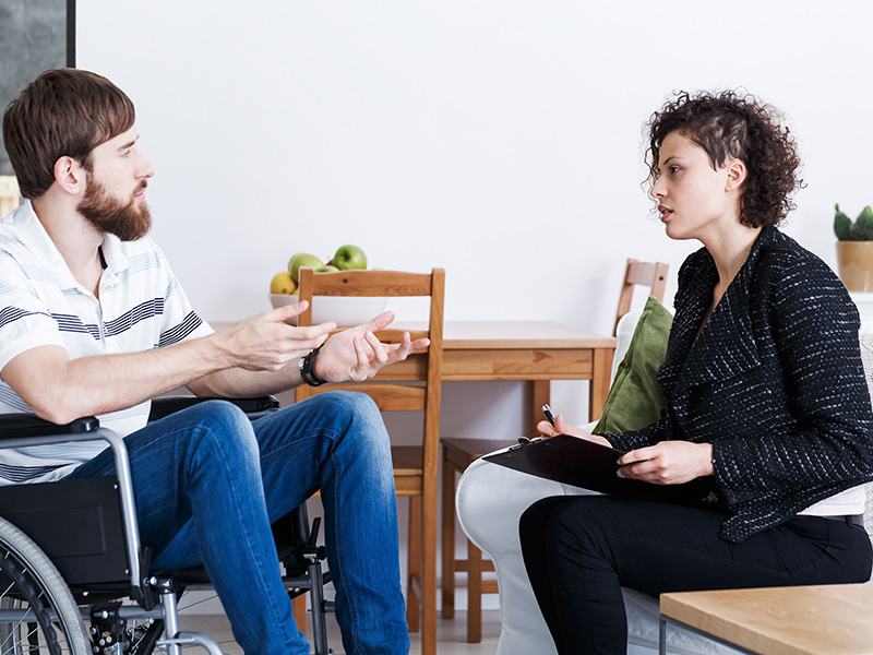 man in wheelchair talking to a social worker holding a clipboard