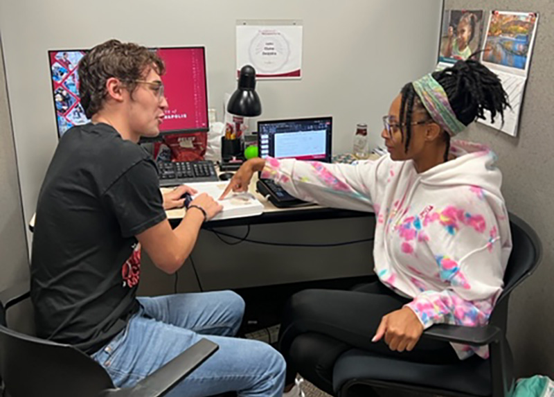 two students talking at a desk