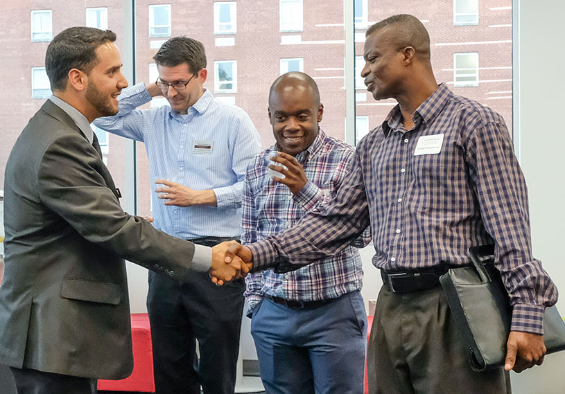 Two men shake hands while two others look on.