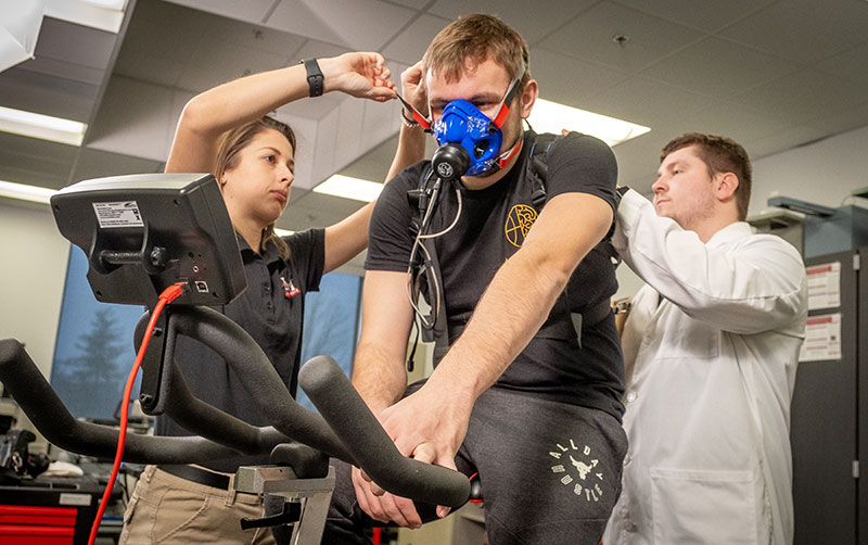 student using equipment on human performance lab while two students assist