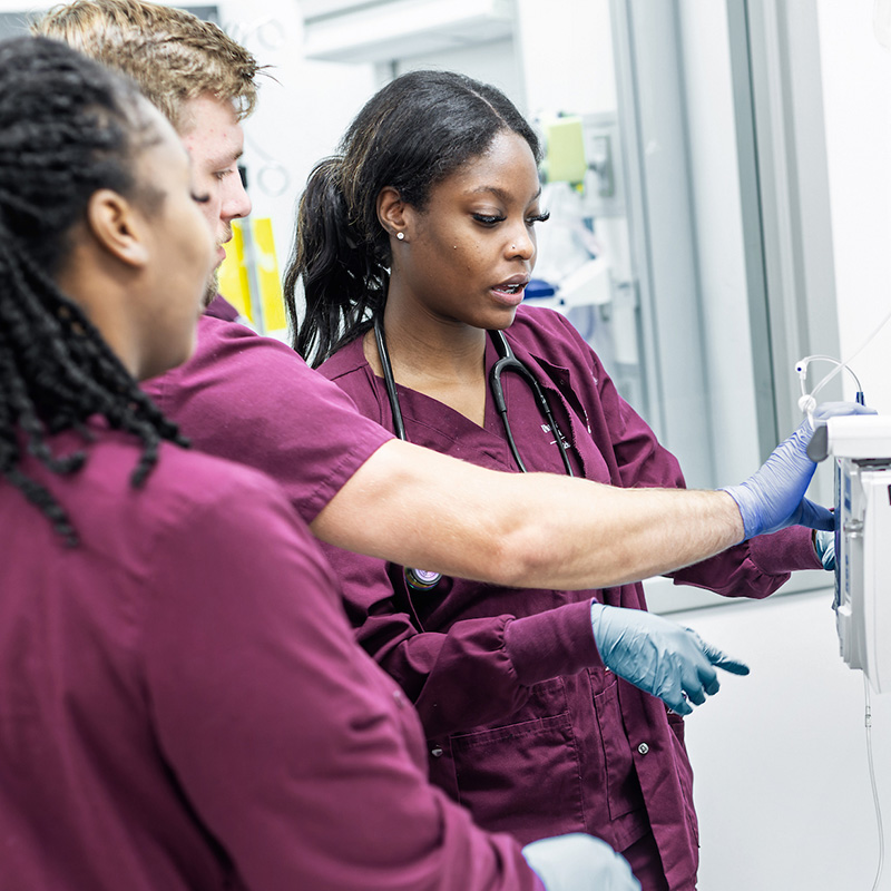 students with red scrubs use nursing equipment