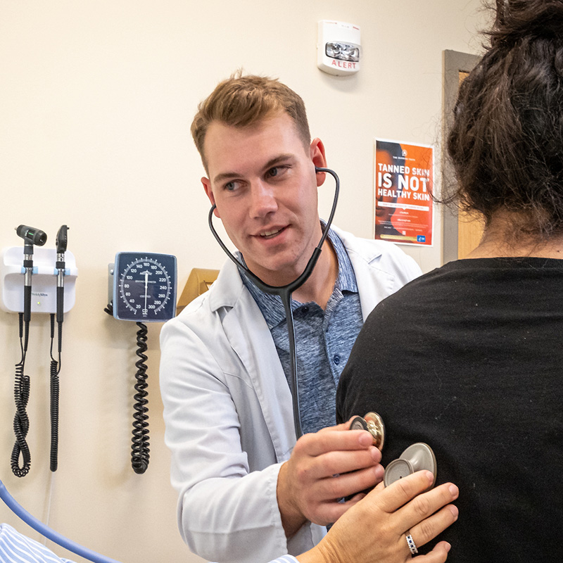 student with white lab coat examines a patient