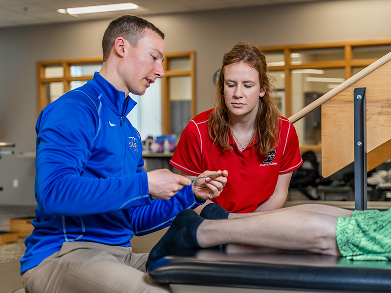 student assists a professional as they perform physical therapy on a client