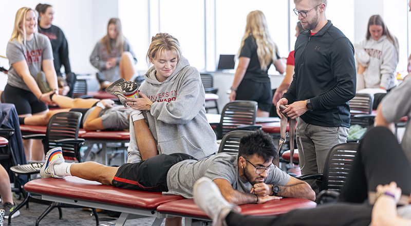 Physical Therapy students practice stretching patients in a medial table in a classroom setting