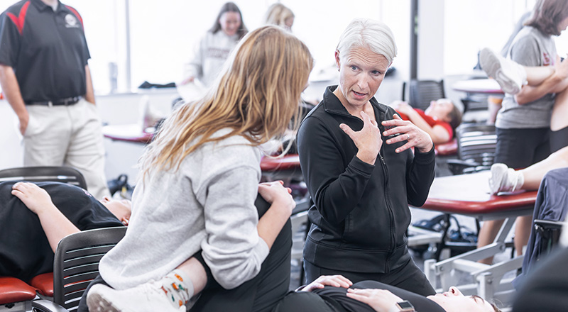 a professor assists a student as they perform physical therapy on a patient