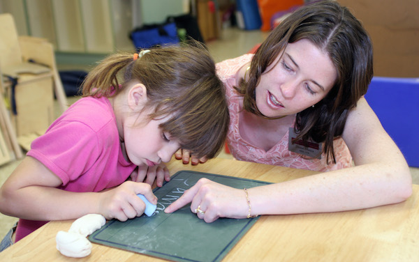 teacher helping a young girl to write on a chalkboard