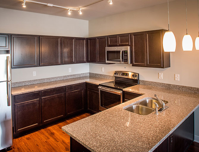 kitchen with a refrigerator, dark cabinets/counter tops, oven, microwave, sink and hanging lights