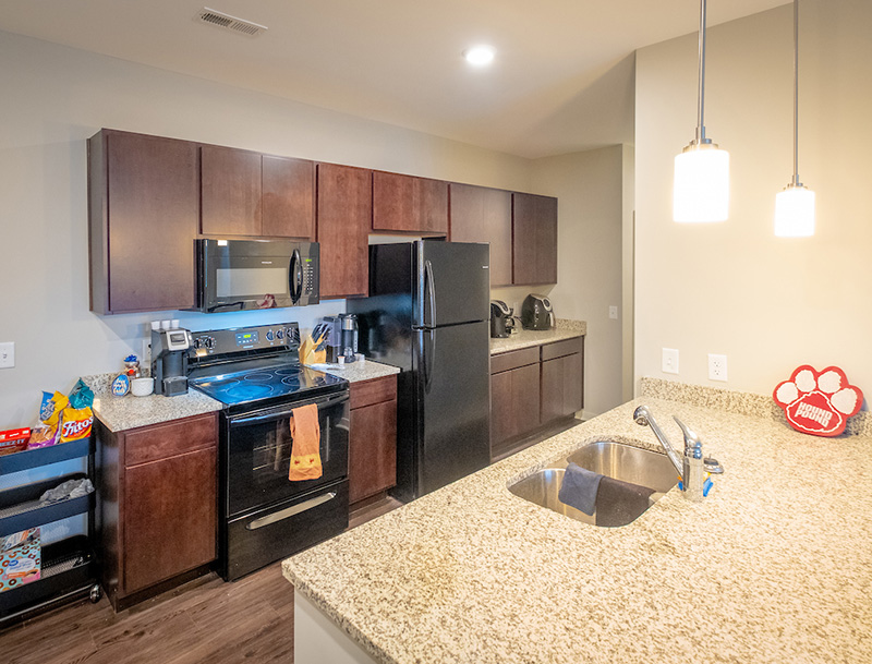 kitchen with dark cabinets, light counter tops, refrigerator, oven, coffee makers, microwave, and sink